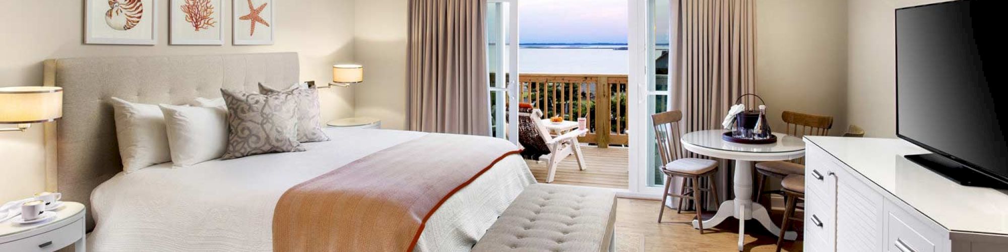 Sanderling Resort's cozy hotel guest room with a bed, artwork, TV, and a sunrise balcony overlooking the atlantic ocean.